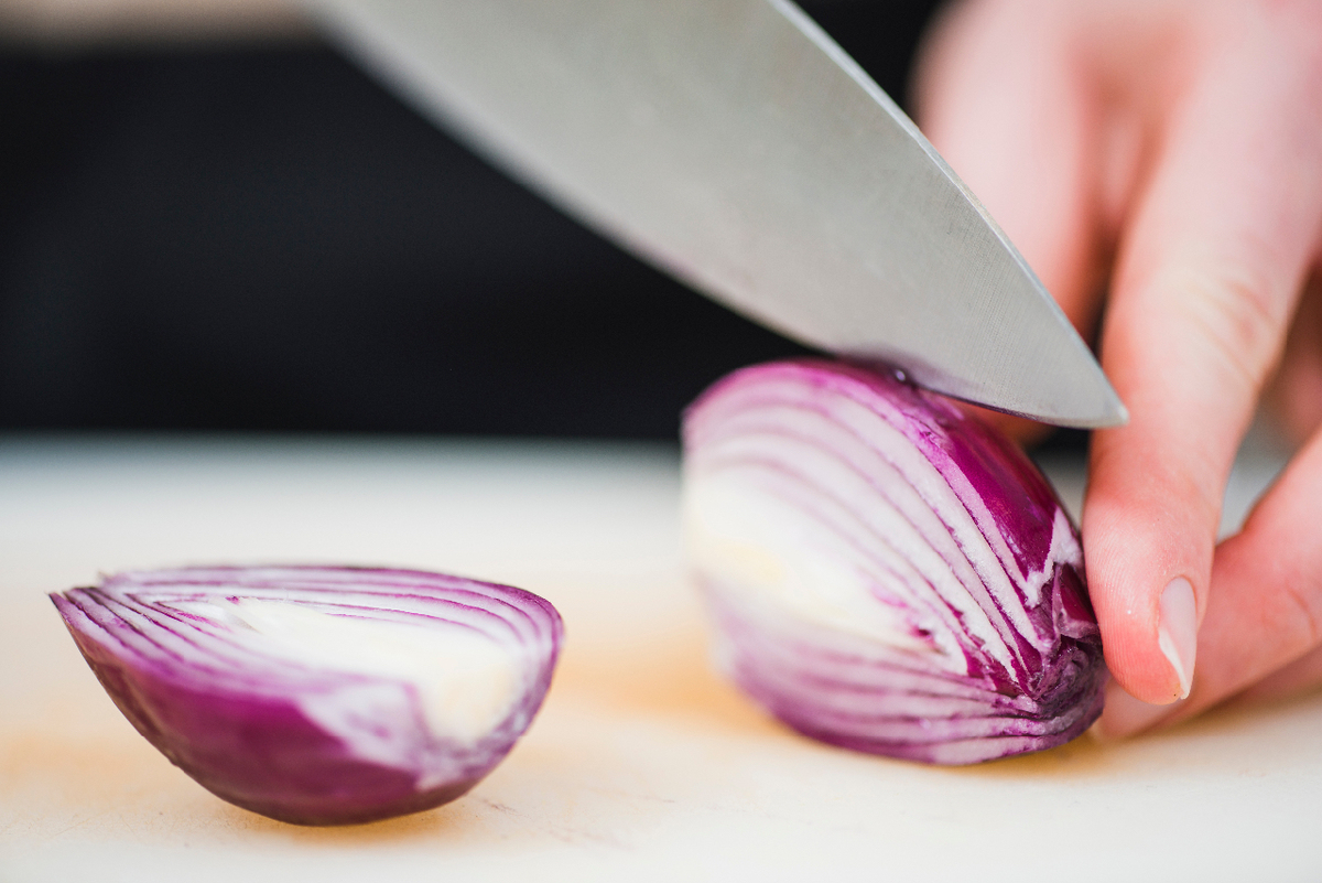 Hands slicing a red onion
